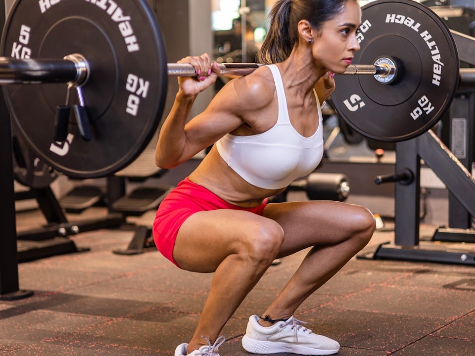 A woman squats in a gym with a barbell